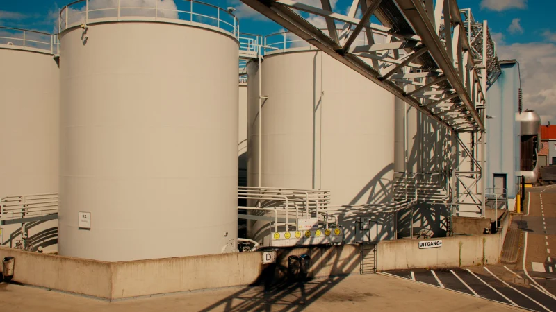 White industrial storage tanks and overhead structure casting shadows