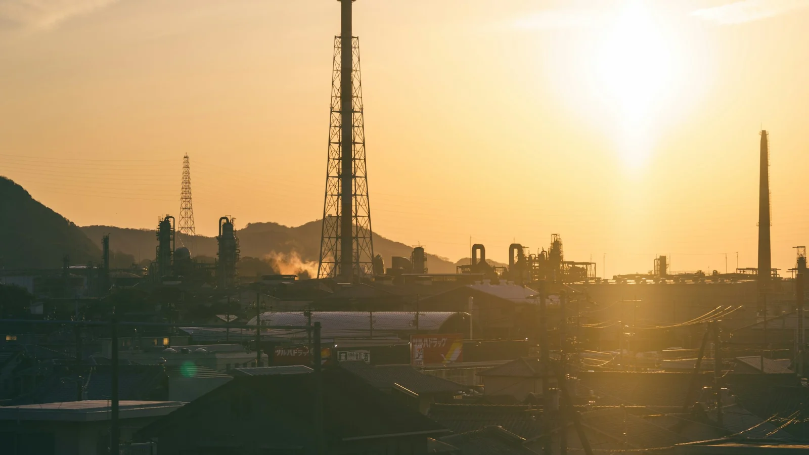 Industrial plant with tall smokestacks silhouetted against a bright warm orange sky